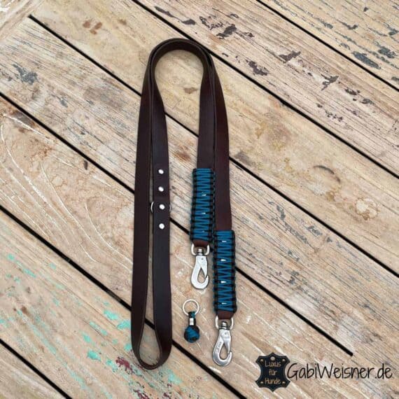 Hundeleine Leder 25 mm breit. 2-fach oder 3-fach verstellbar. Dickes weiches Rindsleder in dunkelbraun. Bestückt mit Edelstahl- oder Messing-Karabiner für große Hunde. Bestückt mit O-Ringen aus Edelstahl oder Messing und unserer Logo-Perle aus Edelstahl. Dekoriert mit unserem Original Knotenmuster im Retro-Look aus Paracord in Braun und Türkis-Blau.