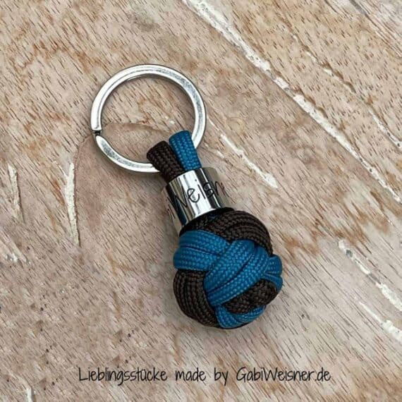 Schlüsselanhänger Ball in Türkis-Blau - Braun. Bestückt mit einem Schlüsselring in silberfarben, innen 2 cm Ø. Gesamtlänge 5 cm. Kleiner Schlüsselanhänger aus Paracord in Form von einem Ball geknotet. Lieferung mit Geschenkverpackung