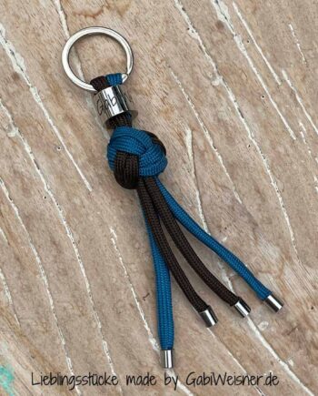 Troddel Schlüsselanhänger in Türkis-Blau - Braun. Bestückt mit einem Schlüsselring in silberfarben, innen 2 cm Ø. Troddel - Schlüsselanhänger aus Paracord in Form von einem Ball geknotet und mit Edelstahl-Endkappen bestückt. Lieferung mit Geschenkverpackung