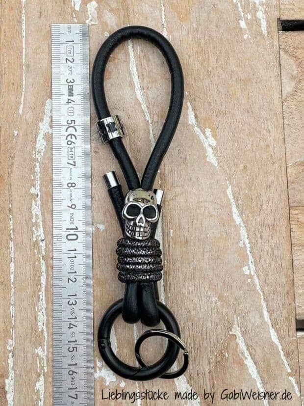 Schlüsselband mit Skull und Karabiner-Ring. 14 cm Nappaleder in Schwarz. Bestückt mit einem Ring-Karabiner in Schwarz. Dekoriert mit hochwertigem Totenkopf, Schlüsselring, Logo-Perle und Edelstahl-Endkappen. Gesamtlänge 16 cm.