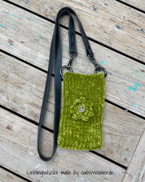 Handytasche zum Umhängen aus Handstrickgarn in der Farbe LIME, Lederriemen in der Farbe GRAU und Metallbeschlag in Schwarzfarben. Große Blume mit Peace